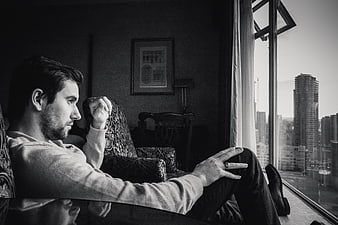 Contemplative young man sitting by window with city view