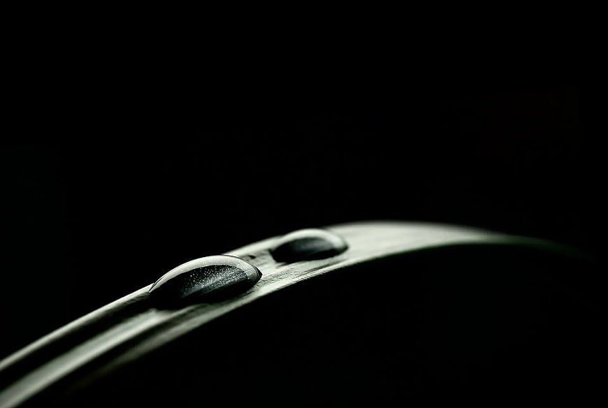 Macro water droplets on green leaf edge against black background