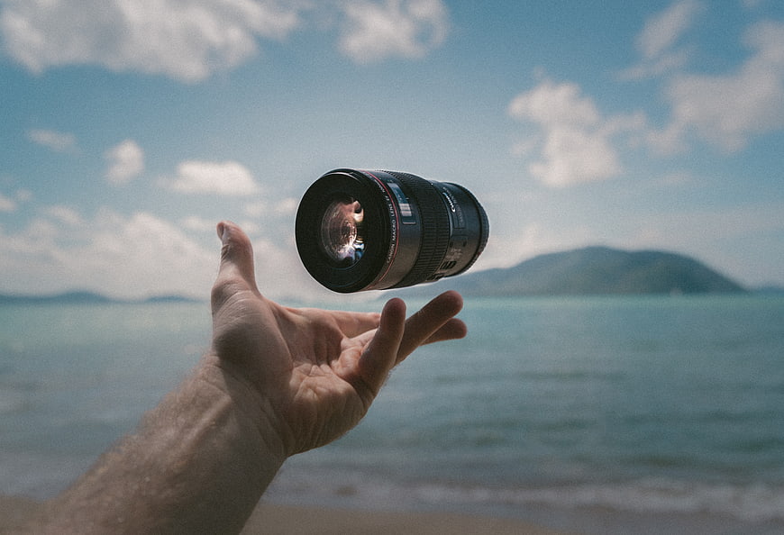 Camera Lens Floating Above Hand on Beach