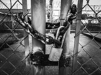 Rusty padlock and heavy chains securing a chain-link fence gate
