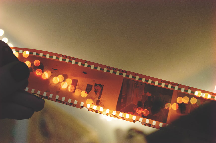 Hand holding vintage film strip with warm bokeh lights