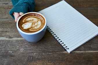 Hand holding latte with notebook on wooden table