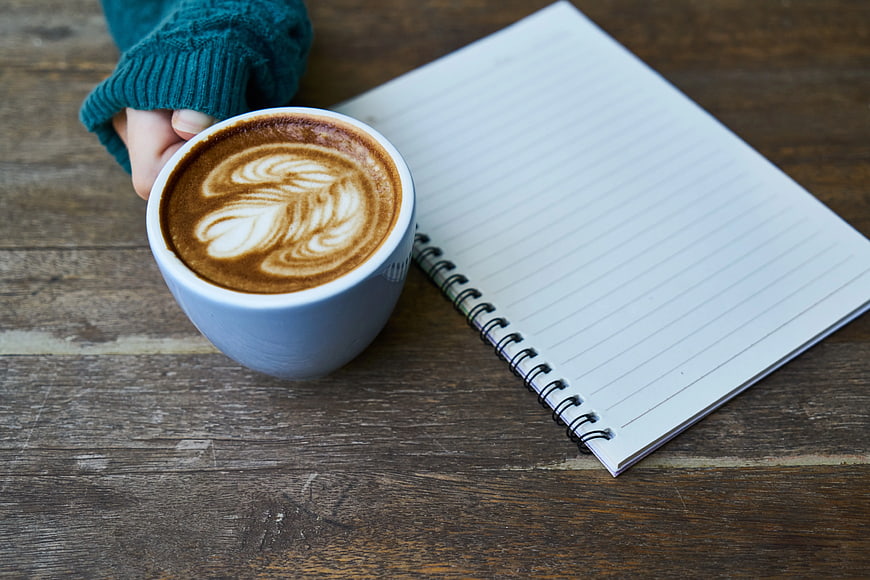 Hand holding latte with notebook on wooden table