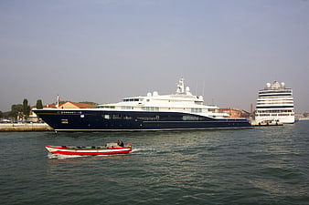 Luxury blue yacht docked in harbor with small red boat