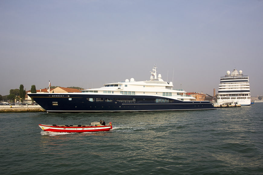 Luxury blue yacht docked in harbor with small red boat