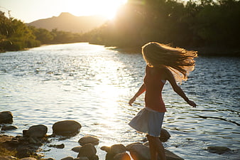 Woman with flowing hair walking by river at sunset