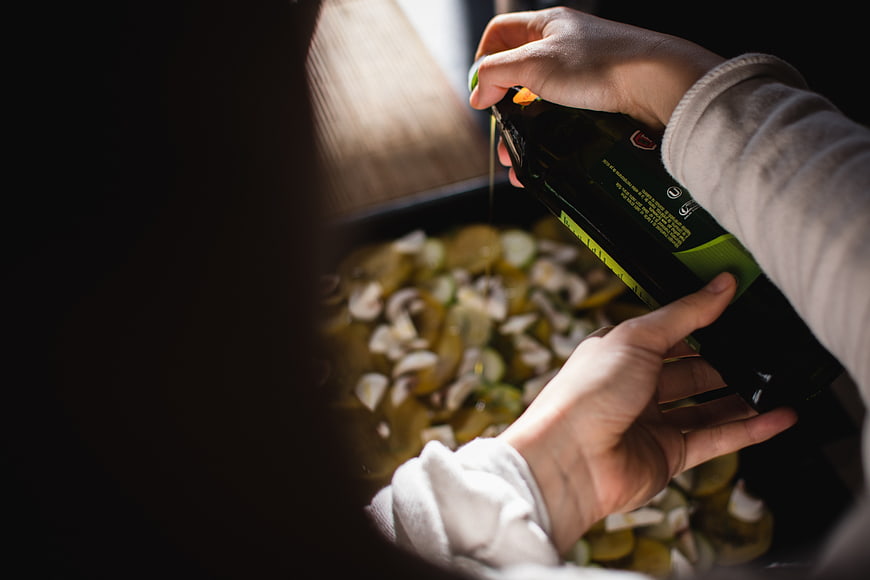 Hands pouring olive oil on roasted vegetables