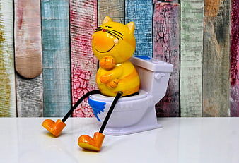 Cute yellow cat figurine sitting on a miniature white toilet