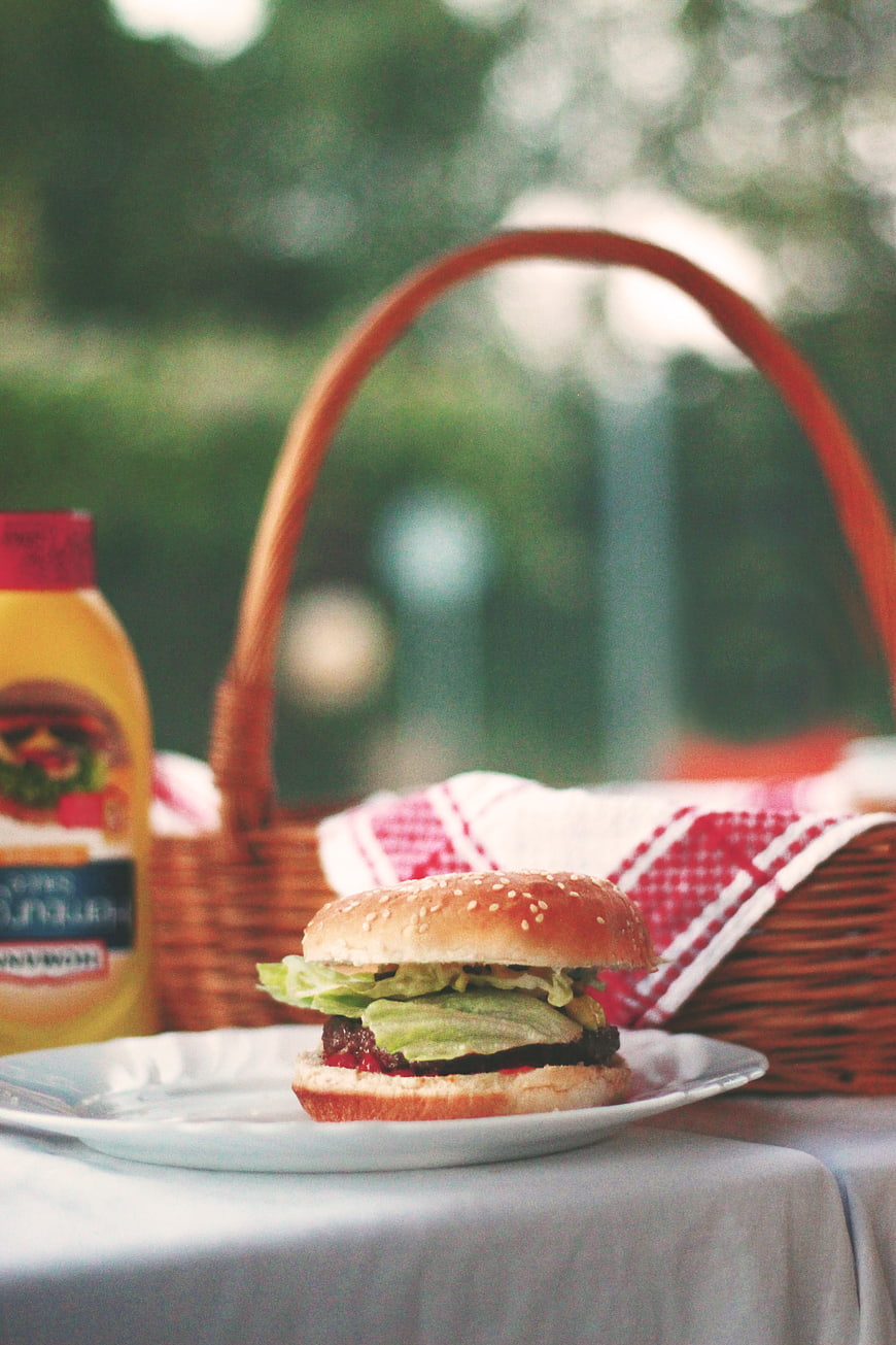 Delicious burger on plate with picnic basket and mustard