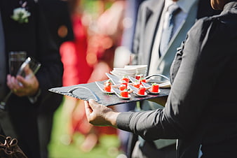 Server presenting gourmet canapés on slate tray at outdoor wedding reception