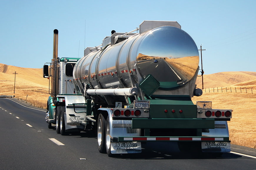 Green semi-truck with shiny tanker driving on highway