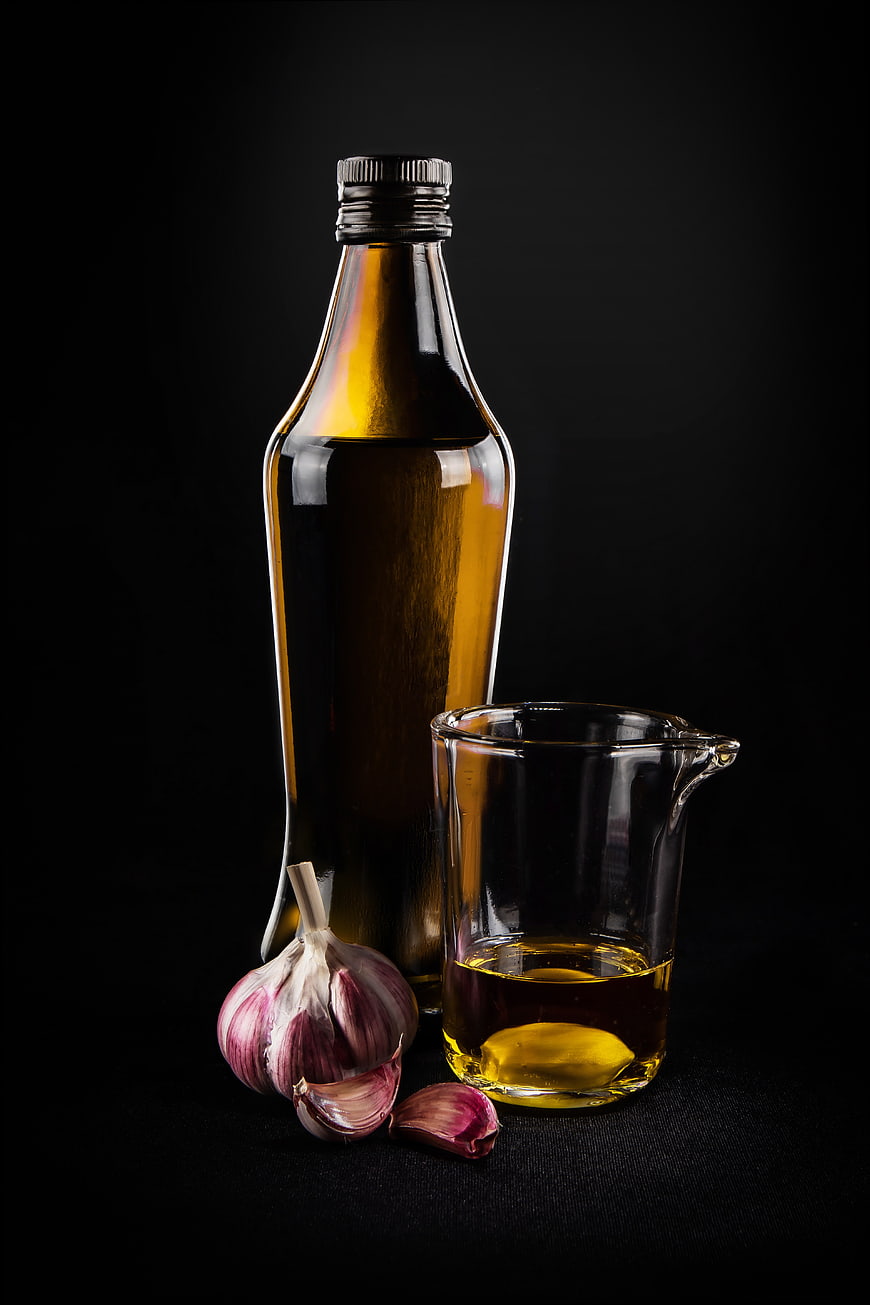 Bottle of olive oil and garlic on black background
