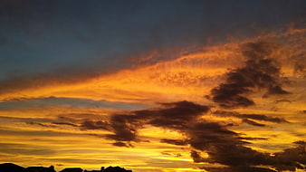 Dramatic orange sunset sky with dark clouds and silhouetted rooftops