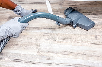Gloved hands vacuuming light wood floor with handheld cleaner