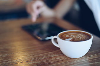 Latte Art Coffee Cup on Wooden Table with Blurred Smartphone