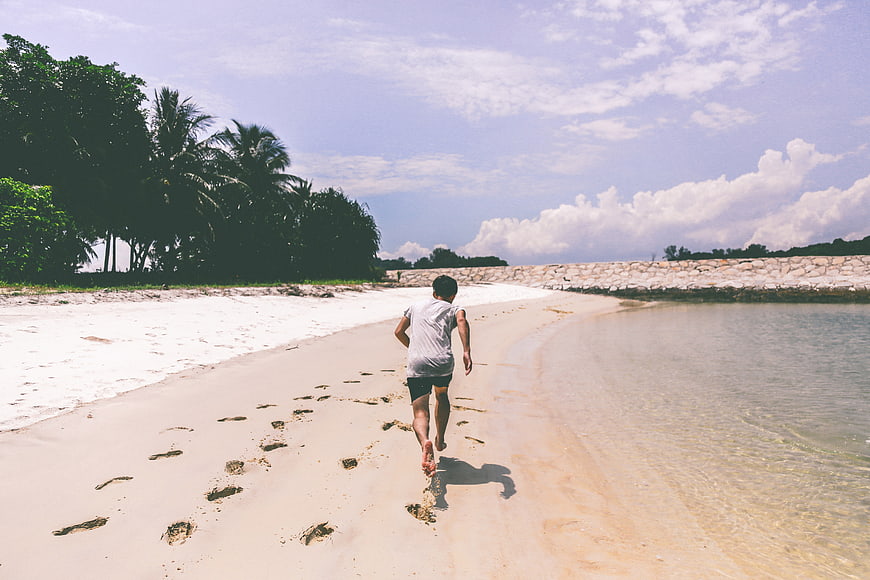 Boy Running Barefoot on Sandy Beach with Footprints