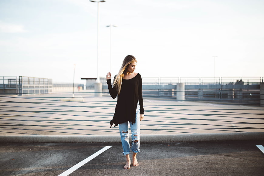 Barefoot woman in black top and ripped jeans walking on parking garage