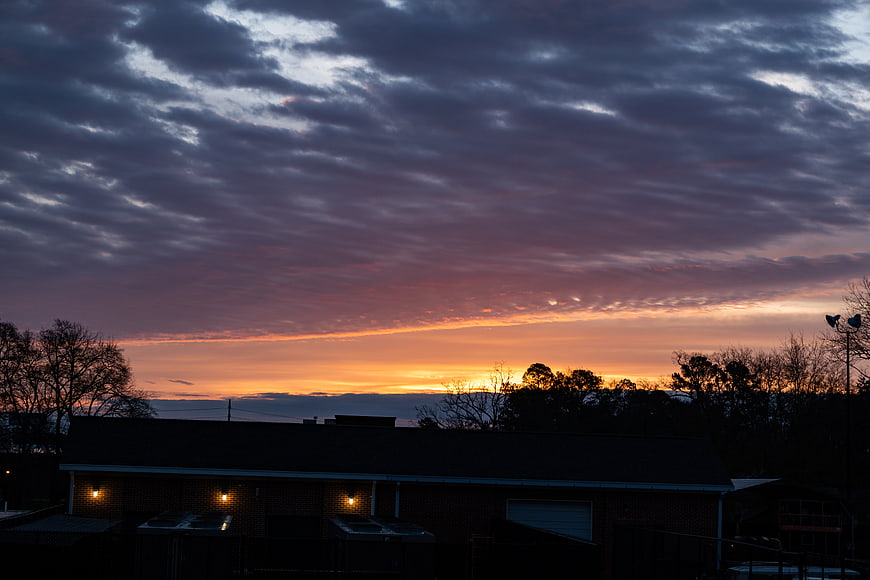 Dramatic sunset sky with clouds over suburban house silhouette