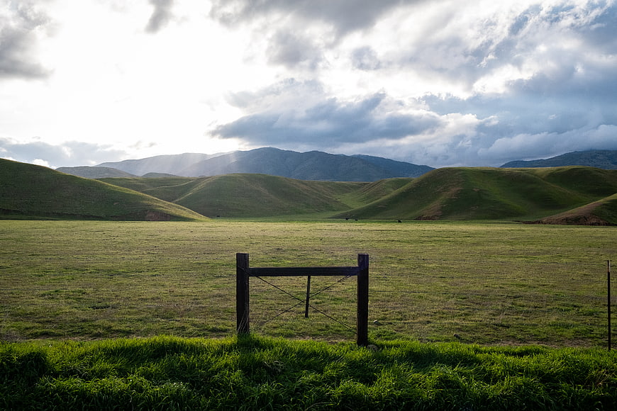 Scenic green valley landscape with wooden gate and dramatic clouds