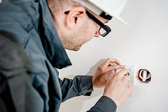 Electrician installing wall socket in white wall
