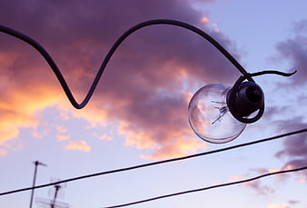 Silhouette of hanging light bulb against colorful sunset sky