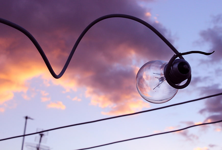 Silhouette of hanging light bulb against colorful sunset sky