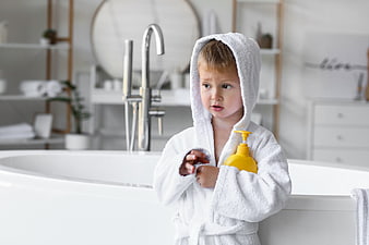 Cute Toddler Boy in White Bathrobe Holding Yellow Soap Bottle