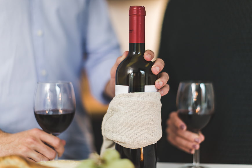 Hands holding red wine bottle and glasses at dinner
