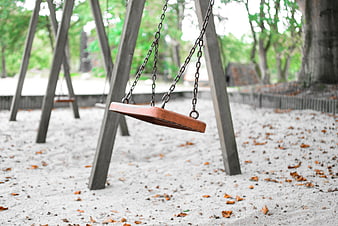 Empty wooden swing in park with sand and fallen leaves