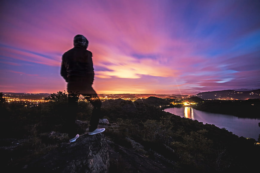 Silhouette of Man Watching Vibrant Sunset Over City and Lake