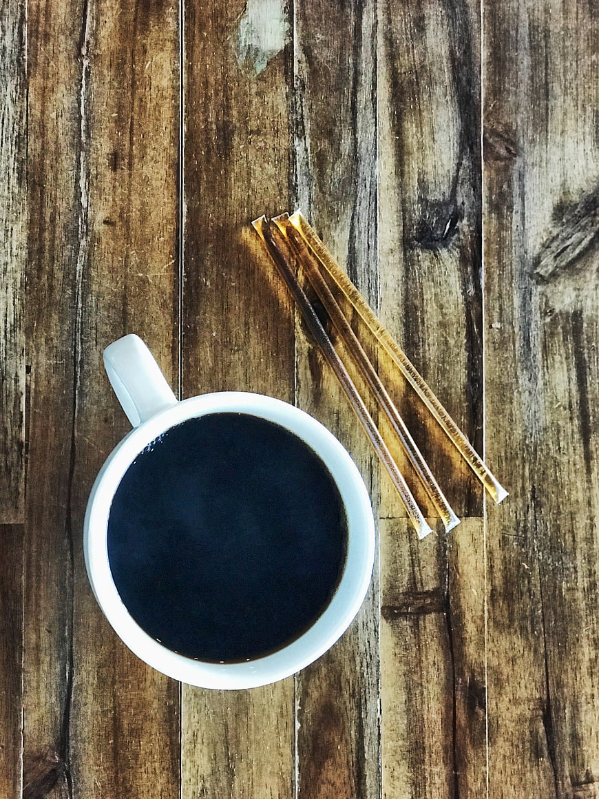 Top View of Black Coffee Cup with Sugar Packets on Rustic Wood