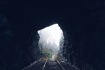 Dark railway tunnel leading to bright forest exit