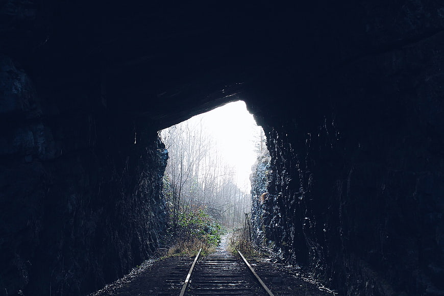 Dark railway tunnel leading to bright forest exit