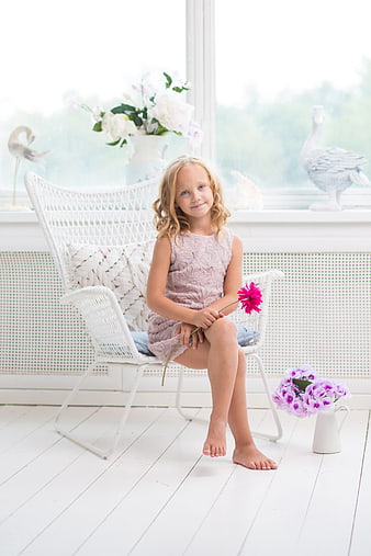 Cute little girl sitting in white chair holding pink flower