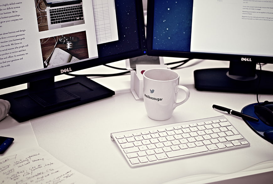 Modern dual monitor workspace with white mug and keyboard