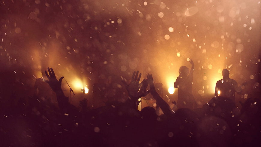 Concert Crowd Silhouettes With Raised Hands And Golden Stage Lights