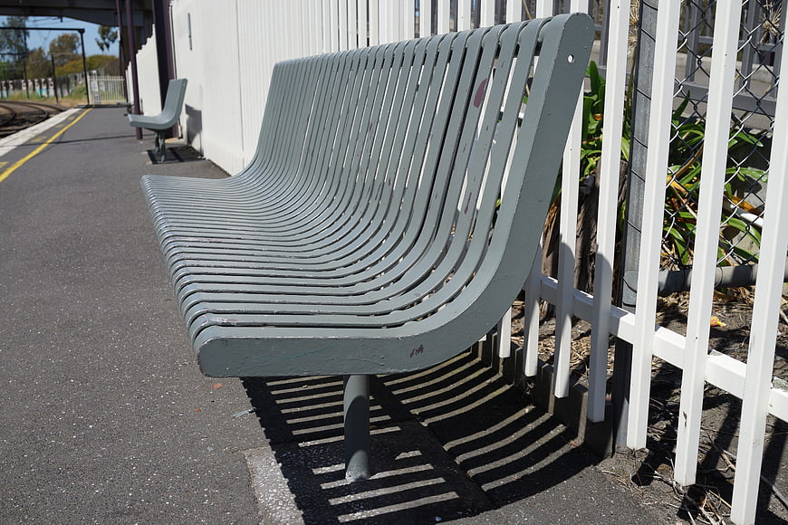 Empty gray metal bench at sunny train station platform