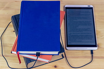 Stack of hardcover books and e-reader tablet on wooden table