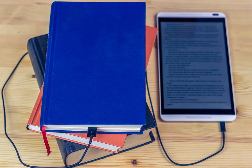 Stack of hardcover books and e-reader tablet on wooden table