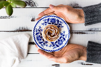 Hands Holding Cinnamon Roll on Blue and White Plate