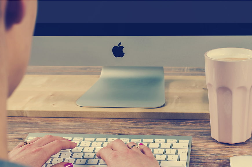 Woman Typing on Apple iMac with Coffee Cup on Desk