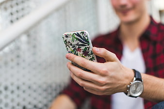 Man holding smartphone with floral case and wristwatch