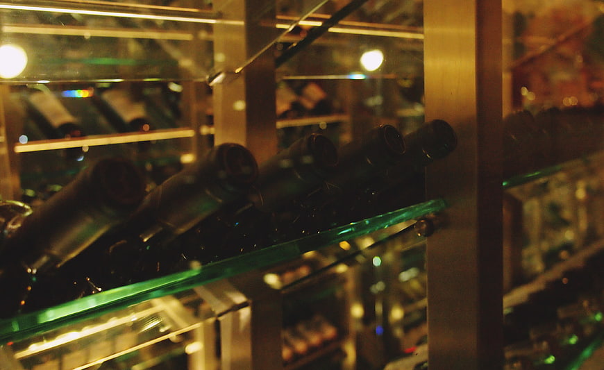 Wine bottles on glass shelves in a dimly lit cellar