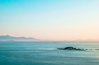 Serene Ocean Landscape with Distant Mountains and Rocky Islet