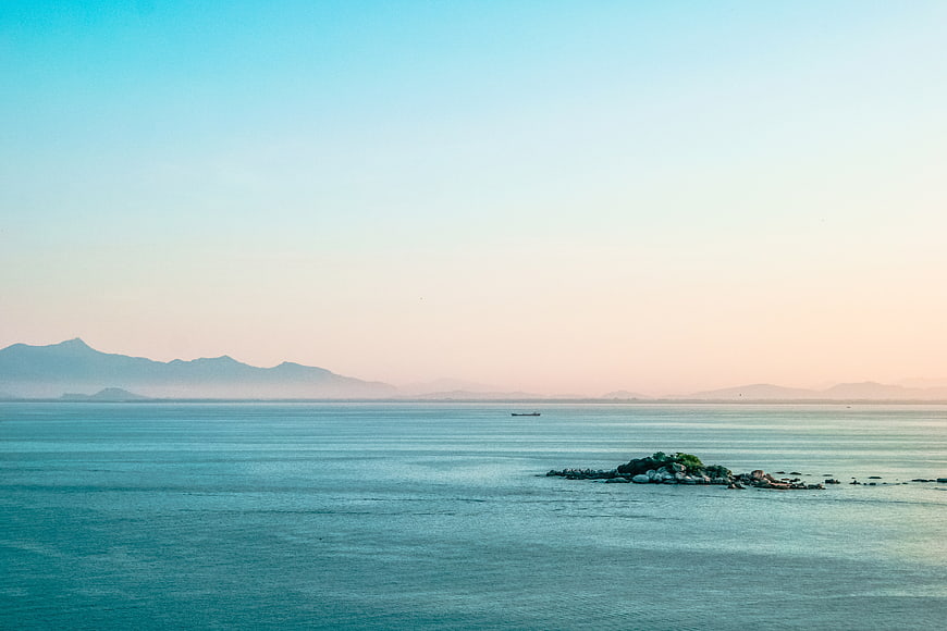 Serene Ocean Landscape with Distant Mountains and Rocky Islet