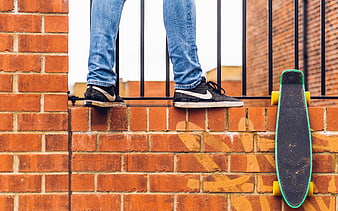 Skateboarder legs on brick wall with longboard