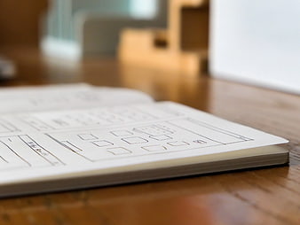 Hand-drawn UI wireframes in a notebook on a wooden desk