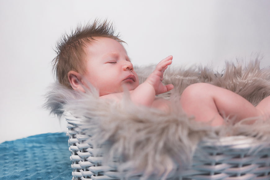 Sleeping newborn baby in white wicker basket with fur