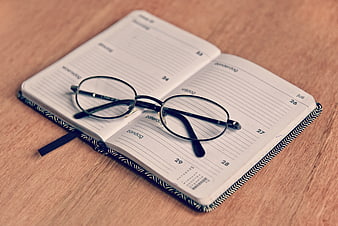 Open weekly planner notebook with eyeglasses on wooden desk
