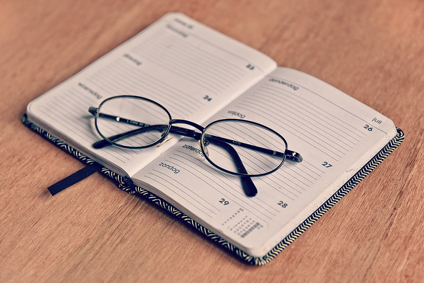 Open weekly planner notebook with eyeglasses on wooden desk